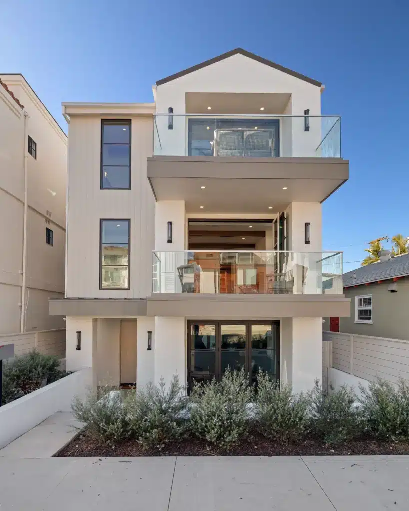 Front elevation of the three-story coastal home with glass balcony railings